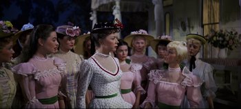 Movie still from “Oklahoma!” (1955), directed by Fred Zinnemann – A group of women standing next to each other in dresses; Medium shot, Over the shoulder angle
