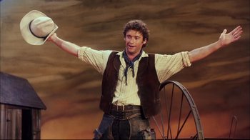 Movie still from “Oklahoma!” (1999), directed by Trevor Nunn – A man standing in front of an old wagon; Medium shot, Low angle