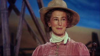 Movie still from “Oklahoma!” (1999), directed by Trevor Nunn – An older woman wearing a straw hat and a pink dress; Close Up shot, Low angle