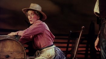 Movie still from “Oklahoma!” (1999), directed by Trevor Nunn – A woman sitting on top of a chair wearing a straw hat; Medium shot, Low angle