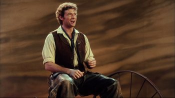 Movie still from “Oklahoma!” (1999), directed by Trevor Nunn – A man sitting on a chair and laughing; Medium shot, Low angle