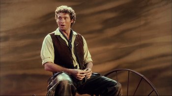 Movie still from “Oklahoma!” (1999), directed by Trevor Nunn – A man sitting on a chair wearing a brown vest; Medium shot, Over the shoulder angle