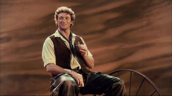 Movie still from “Oklahoma!” (1999), directed by Trevor Nunn – A man sitting on a chair holding a cell phone; Medium shot, Low angle