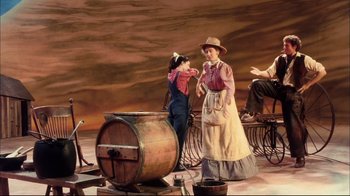 Movie still from “Oklahoma!” (1999), directed by Trevor Nunn – A woman and a child are standing next to a barrel; Wide shot, High angle