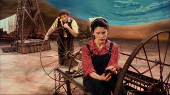 Movie still from “Oklahoma!” (1999), directed by Trevor Nunn – A man and a woman sitting in a field; Wide shot, High angle
