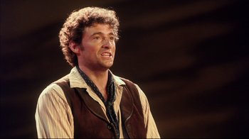 Movie still from “Oklahoma!” (1999), directed by Trevor Nunn – A man with curly brown hair and a brown vest; Close Up shot, Over the shoulder angle