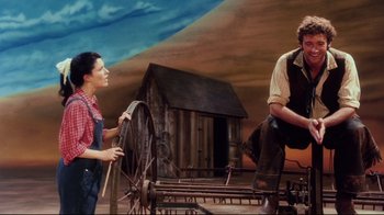 Movie still from “Oklahoma!” (1999), directed by Trevor Nunn – A man and a woman are standing in front of an old barn; Wide shot, Low angle