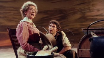 Movie still from “Oklahoma!” (1999), directed by Trevor Nunn – A man and a woman sitting next to each other in front of a pot; Medium shot, Over the shoulder angle