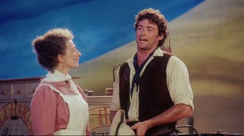 Movie still from “Oklahoma!” (1999), directed by Trevor Nunn – A man and a woman are standing next to each other; Medium shot, Over the shoulder angle