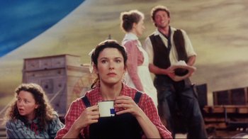 Movie still from “Oklahoma!” (1999), directed by Trevor Nunn – A woman holding a cup while standing next to two other people; Medium shot, Low angle