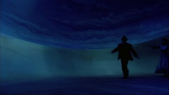 Movie still from “Oklahoma!” (1999), directed by Trevor Nunn – A man in a suit and hat walking in the dark; Extreme Wide shot, Low angle
