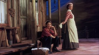 Movie still from “Oklahoma!” (1999), directed by Trevor Nunn – Two women dressed in old time clothing on a porch; Wide shot, Low angle