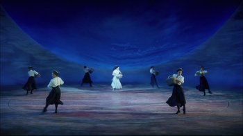 Movie still from “Oklahoma!” (1999), directed by Trevor Nunn – A group of people standing on a stage holding parasols; Extreme Wide shot, High angle