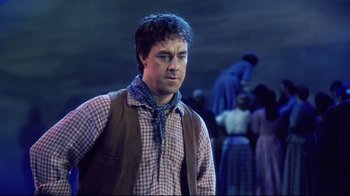 Movie still from “Oklahoma!” (1999), directed by Trevor Nunn – A man standing in front of a group of people; Medium shot, Low angle