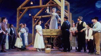 Movie still from “Oklahoma!” (1999), directed by Trevor Nunn – A group of people standing in front of a wooden structure; Wide shot, Low angle
