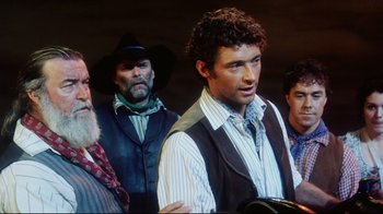 Movie still from “Oklahoma!” (1999), directed by Trevor Nunn – A group of men standing next to each other; Medium shot, Over the shoulder angle