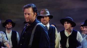 Movie still from “Oklahoma!” (1999), directed by Trevor Nunn – A group of men in hats and vests standing next to each other; Medium shot, Low angle