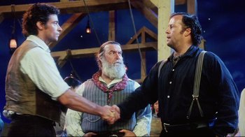 Movie still from “Oklahoma!” (1999), directed by Trevor Nunn – Two men shake hands while another man looks on; Medium shot, Over the shoulder angle