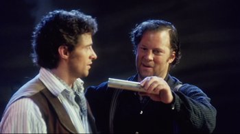 Movie still from “Oklahoma!” (1999), directed by Trevor Nunn – A man holding a video game controller talking to another man in front of him; Close Up shot, Over the shoulder angle