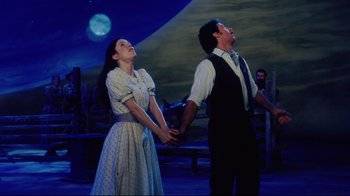 Movie still from “Oklahoma!” (1999), directed by Trevor Nunn – A man and a woman holding hands in front of the moon; Medium shot, Low angle