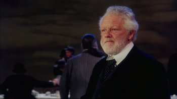 Movie still from “Oklahoma!” (1999), directed by Trevor Nunn – An older man in a black suit and a white beard; Close Up shot, Low angle