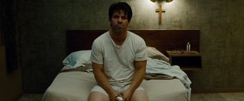 Movie still from “Oldboy” (2013), directed by Spike Lee – A man sitting on top of a bed holding a remote control; Medium shot, High angle