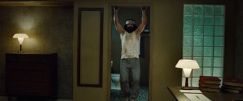 Movie still from “Oldboy” (2013), directed by Spike Lee – A man with a beard is doing a pull - up; Medium shot, Low angle