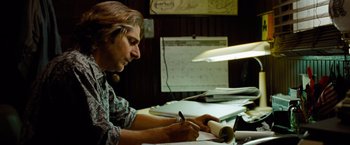 Movie still from “Oldboy” (2013), directed by Spike Lee – A man sitting at a desk writing on a piece of paper; Medium shot, Low angle