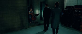 Movie still from “Oldboy” (2013), directed by Spike Lee – A woman playing the cello in a dark room with two men; Wide shot, Over the shoulder angle