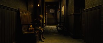 Movie still from “Oliver Twist” (2005), directed by Roman Polanski – A person sitting on a bench in a dark hallway; Wide shot, High angle
