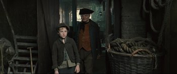 Movie still from “Oliver Twist” (2005), directed by Roman Polanski – A man standing next to a young boy in front of a basket of potatoes; Medium shot, Over the shoulder angle