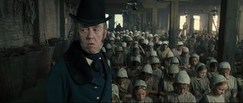 Movie still from “Oliver Twist” (2005), directed by Roman Polanski – An old man in a hat standing in front of a group of people; Medium shot, Low angle