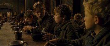 Movie still from “Oliver Twist” (2005), directed by Roman Polanski – A group of people sitting at a table eating food; Medium shot, High angle