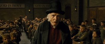 Movie still from “Oliver Twist” (2005), directed by Roman Polanski – An old man wearing a top hat in front of a group of people; Medium shot, Low angle