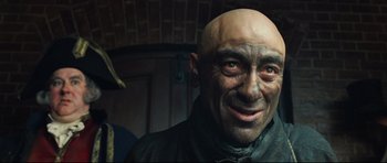 Movie still from “Oliver Twist” (2005), directed by Roman Polanski – A man with a bald head is smiling for the camera; Close Up shot, Over the shoulder angle
