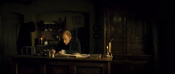 Movie still from “Oliver Twist” (2005), directed by Roman Polanski – An older man sitting at a desk writing on a piece of paper; Medium shot, High angle