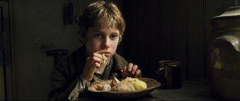 Movie still from “Oliver Twist” (2005), directed by Roman Polanski – A young boy sitting in front of a plate of food; Close Up shot, High angle