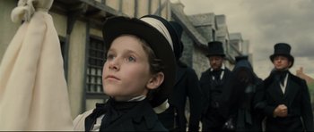 Movie still from “Oliver Twist” (2005), directed by Roman Polanski – A young boy wearing a top hat in front of two men in suits; Close Up shot, Low angle