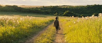 Movie still from “Oliver Twist” (2005), directed by Roman Polanski – A person walking down a dirt road in a grassy field; Extreme Wide shot, Low angle