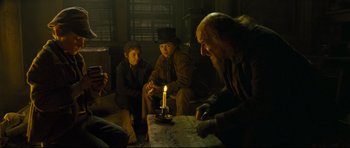 Movie still from “Oliver Twist” (2005), directed by Roman Polanski – A group of people sitting around a table with a lit candle; Medium shot, Over the shoulder angle
