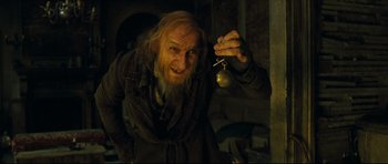 Movie still from “Oliver Twist” (2005), directed by Roman Polanski – An old man holding a bell in a dark room; Medium shot, High angle