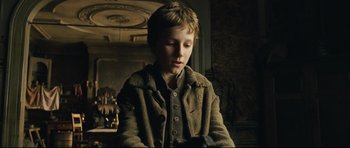 Movie still from “Oliver Twist” (2005), directed by Roman Polanski – A young boy in a brown jacket looking down; Medium shot, Over the shoulder angle