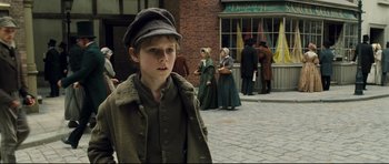 Movie still from “Oliver Twist” (2005), directed by Roman Polanski – A young boy wearing a hat and a coat; Medium shot, Over the shoulder angle