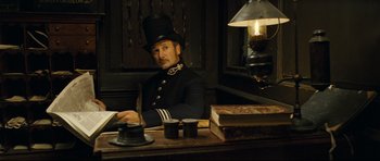 Movie still from “Oliver Twist” (2005), directed by Roman Polanski – A man sitting at a desk wearing a top hat; Medium shot, Low angle