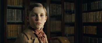 Movie still from “Oliver Twist” (2005), directed by Roman Polanski – A young boy in a suit and tie in front of a book shelf; Close Up shot, Low angle