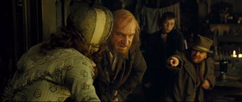 Movie still from “Oliver Twist” (2005), directed by Roman Polanski – A man with long hair and a beard is talking to two other people; Medium shot, Over the shoulder angle