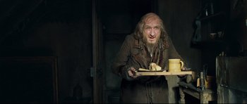 Movie still from “Oliver Twist” (2005), directed by Roman Polanski – An old man holding a piece of bread in his hand; Medium shot, Over the shoulder angle