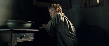 Movie still from “Oliver Twist” (2005), directed by Roman Polanski – A young boy sitting at a table with a glass of water; Medium shot, Low angle