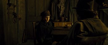 Movie still from “Oliver Twist” (2005), directed by Roman Polanski – A person sitting on a chair in a dark room; Medium shot, Over the shoulder angle