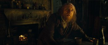 Movie still from “Oliver Twist” (2005), directed by Roman Polanski – A man with a long beard is sitting at a table; Medium shot, Over the shoulder angle